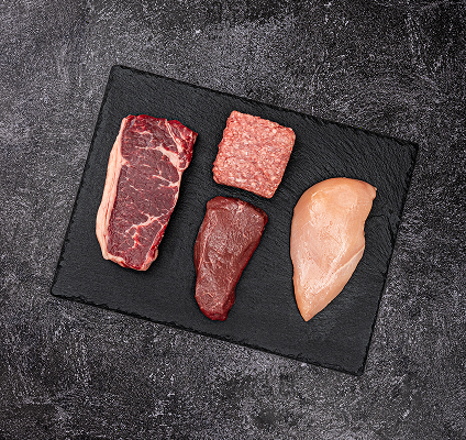 Assorted raw meats on a black slate surface