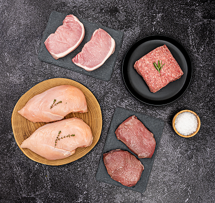 Assorted raw meats including chicken breasts, pork chops, and ground beef on a dark surface.