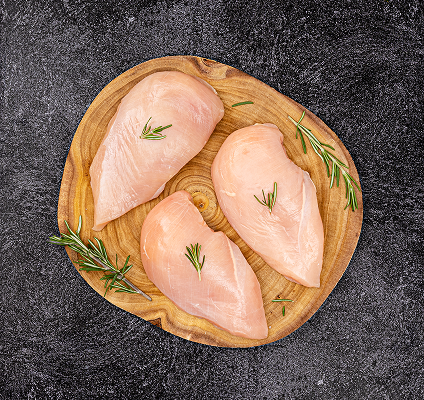 Three raw chicken breasts on a wooden cutting board with rosemary sprigs on a dark surface