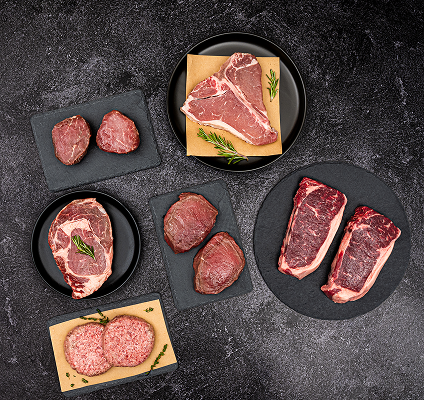 Assorted raw steaks on black slate plates with a dark background