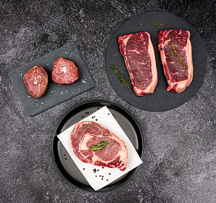 Raw steaks on black slate plates with salt and pepper.